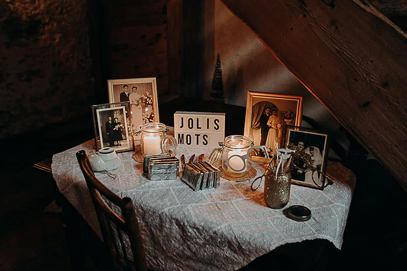 Table de souvenirs romantique avec photos de couple, bougies et petit mot Jolis Mots sur une nappe en dentelle blanche.