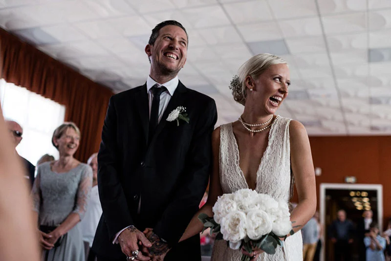 Jeunes mariés souriants, lui en costume noir et elle en robe blanche avec un bouquet de pivoines, lors de leur union.