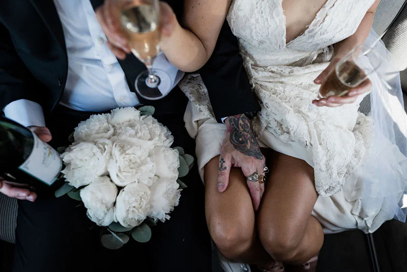 Couple de mariés trinquant avec du champagne, entourés d'un bouquet de pivoines blanches.