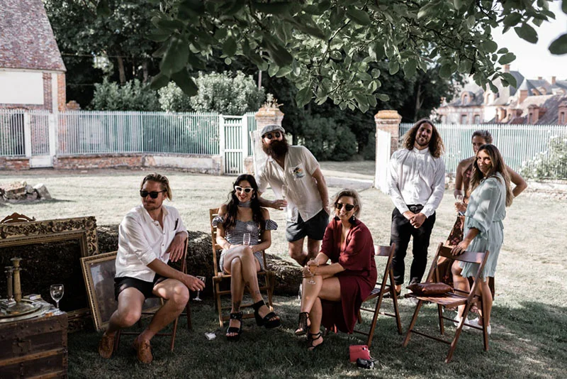 Groupe d'amis décontractés posant en extérieur dans un jardin avec des cadres anciens et un style bohème.