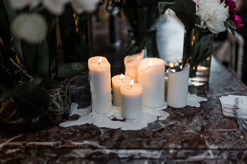 Bougies blanches allumées et coulures de cire sur une table en marbre brun, ambiance romantique et tamisée.