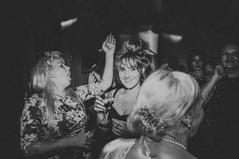 Femmes festoyant avec enthousiasme lors d'une soirée de mariage, cliché en noir et blanc à l'ambiance dynamique.