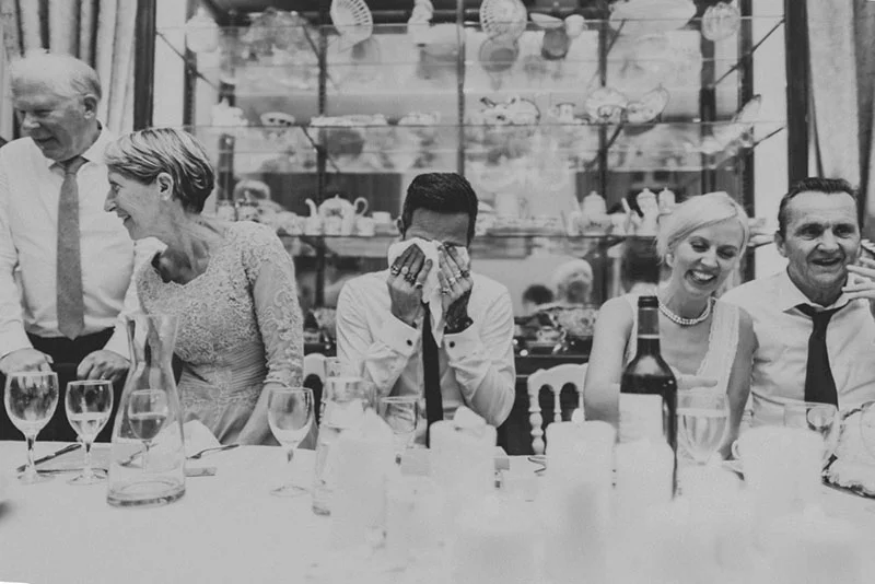 Photo noir et blanc d'invités riant et s'émouvant à table lors du mariage de Jade et Sully.