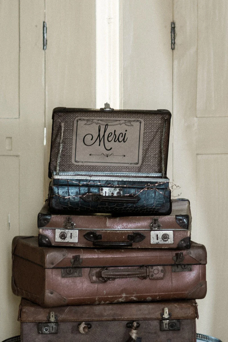 Pile de valises vintage en cuir brun avec une mallette ouverte affichant le mot Merci.