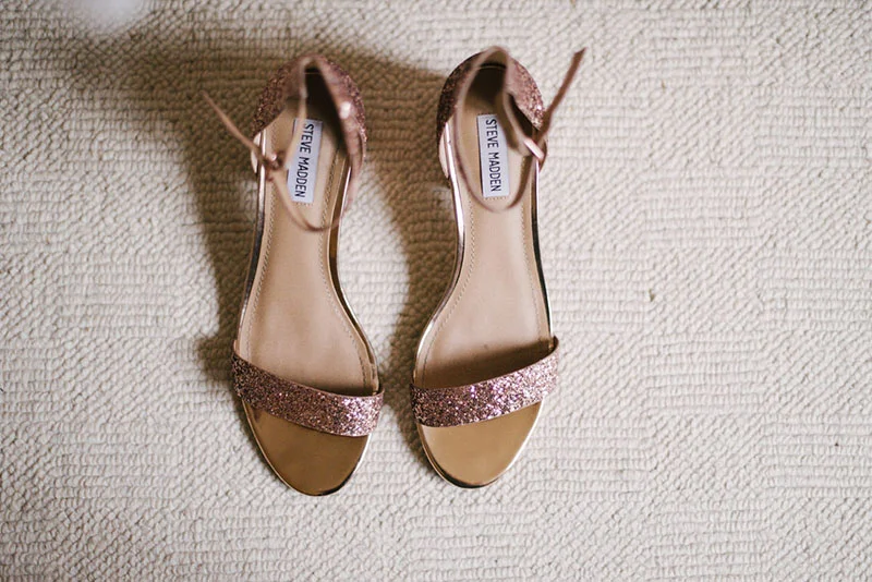 Paire de sandales à talons scintillantes rose gold posées sur un tapis blanc.