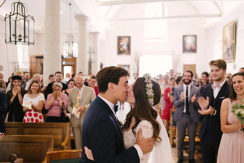Mélanie et Jonathan s'embrassent devant leurs invités dans une église lumineuse lors de leur cérémonie de mariage.