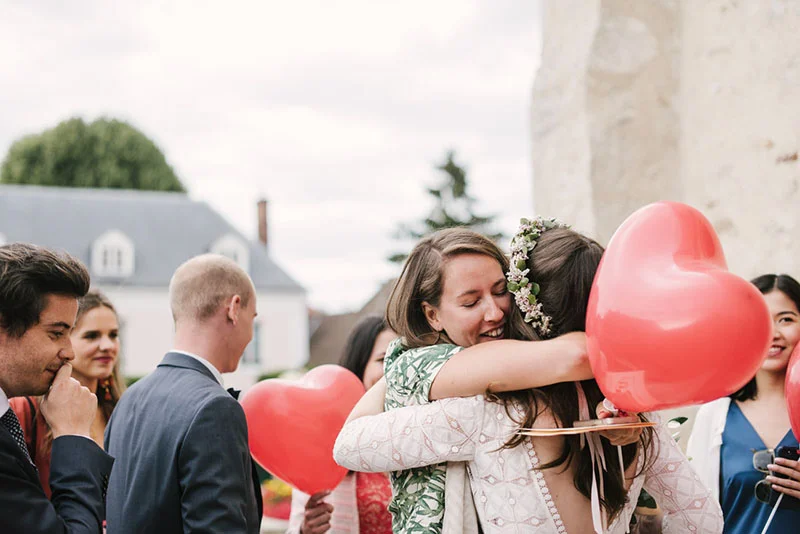 Une mariée et son amie s'embrassent chaleureusement lors d'une réception en plein air avec des ballons rouges en cœur.