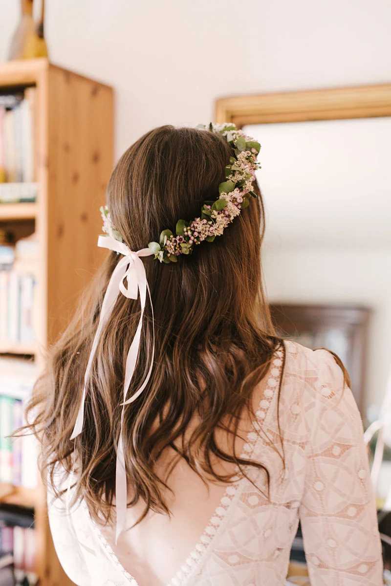 Vue de dos d'une mariée aux cheveux ondulés portant une couronne de fleurs et une robe en dentelle blanche.