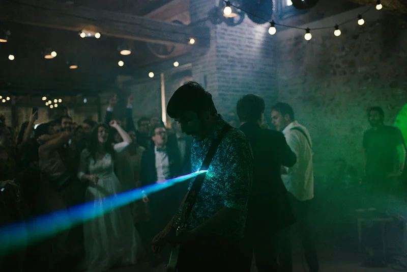 Musicien jouant de la guitare lors d'une soirée de mariage festive avec jeux de lumières bleues et vertes.