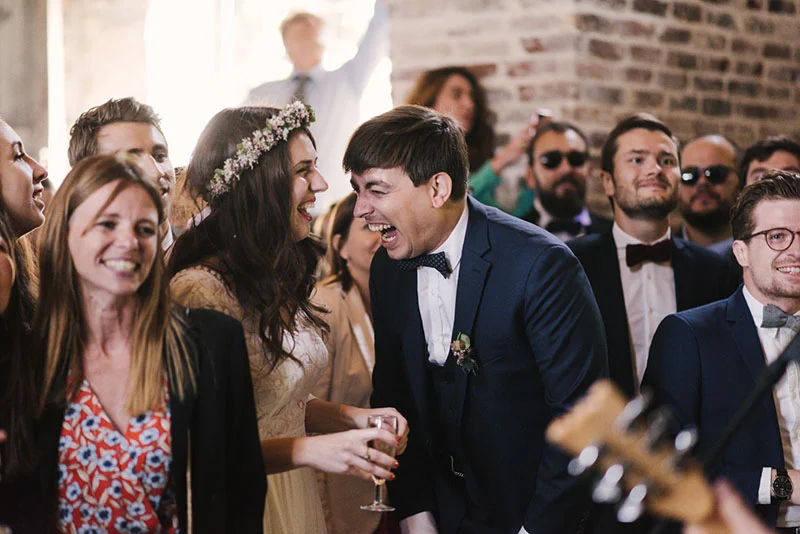 Mélanie et Jonathan rient avec leurs invités lors d'une réception de mariage chaleureuse et festive.