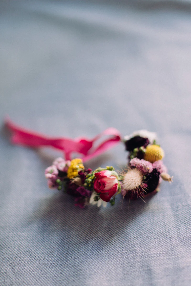 Couronne de fleurs miniatures colorées avec un ruban rose posée sur un tissu bleu clair.
