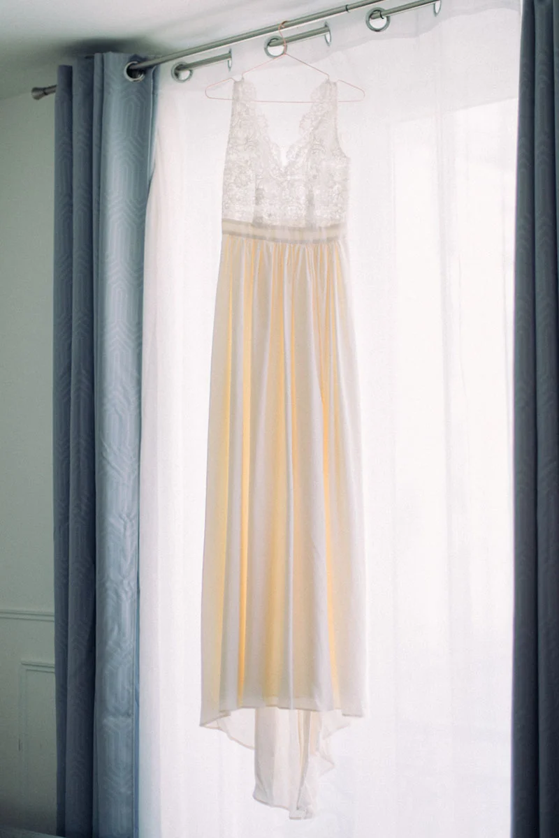 Robe de mariée blanche et crème suspendue devant un rideau lumineux, ambiance douce et romantique.