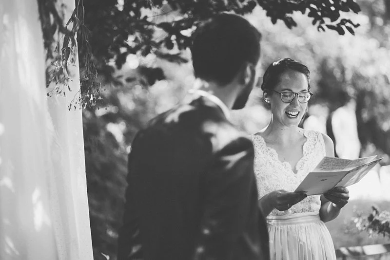Photo noir et blanc de Clara lisant ses vœux à Julien lors de leur cérémonie de mariage en extérieur.
