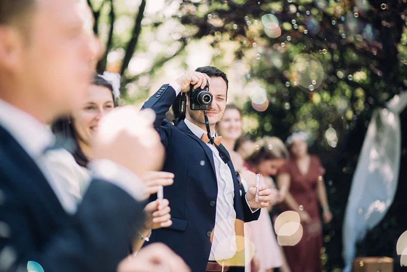Un invité en costume bleu prend une photo lors du mariage de Clara et Julien dans une ambiance festive et lumineuse.