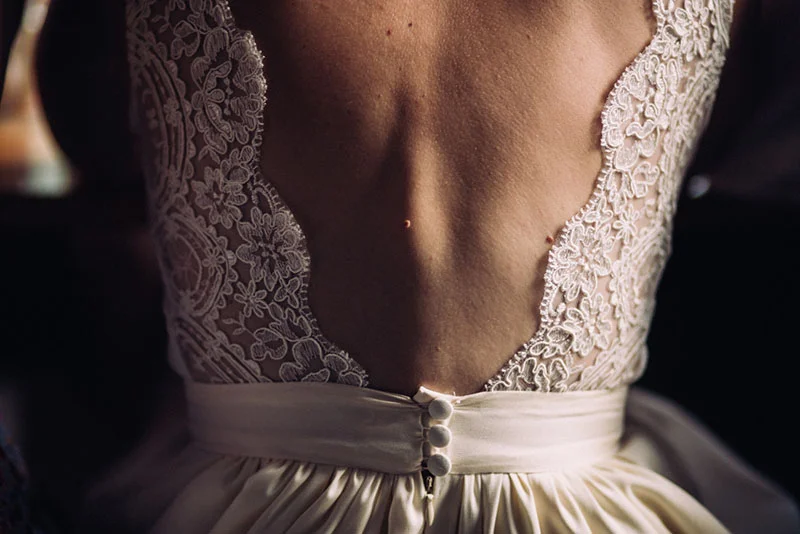 Dos nu d'une robe de mariée en dentelle blanche avec boutons satinés, ambiance douce et romantique.