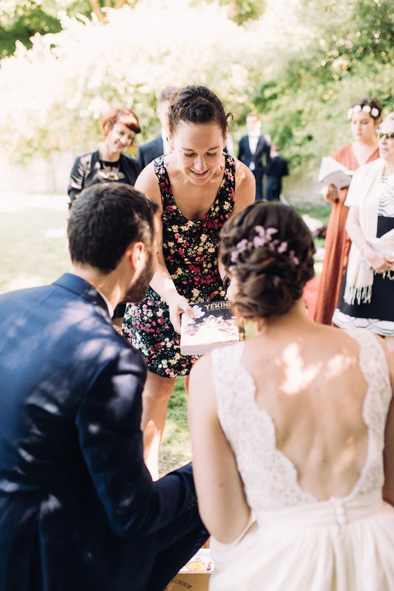 Une invitée offre un cadeau à Clara et Julien lors de leur mariage en plein air dans une ambiance chaleureuse.