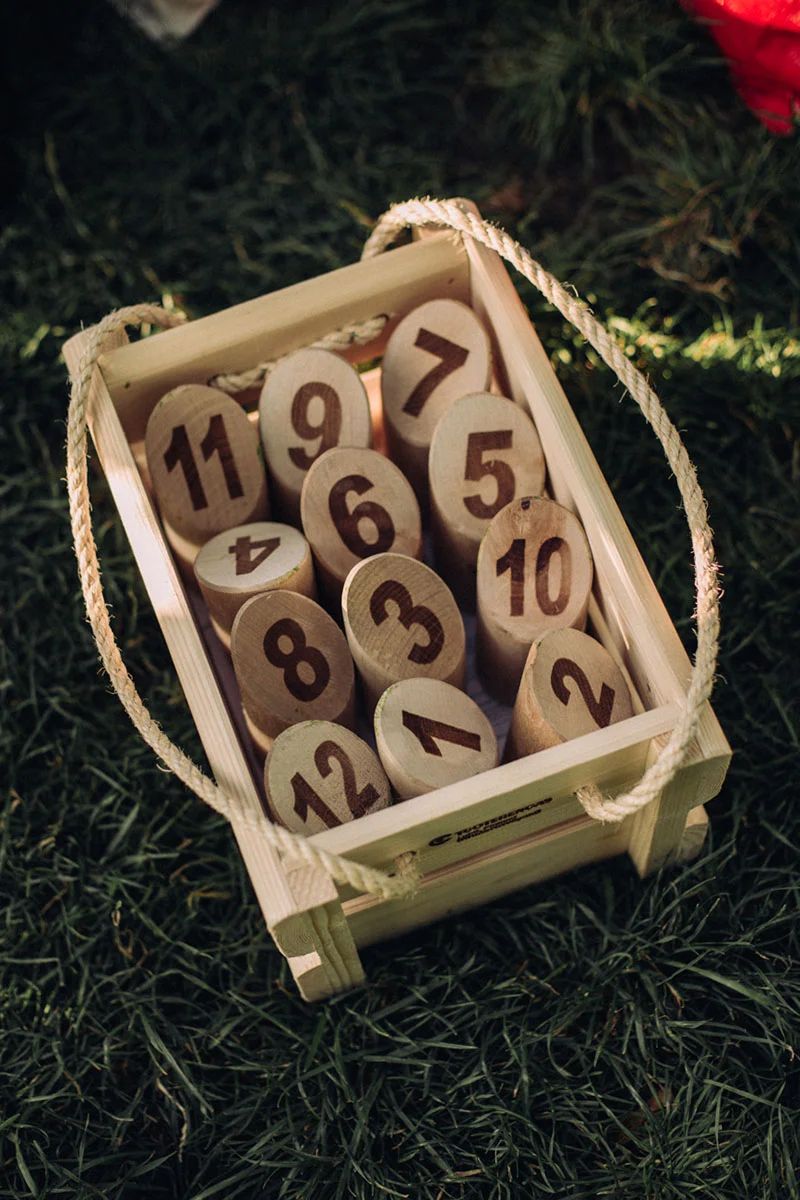 Numéros de table en bois brûlé disposés dans un petit bac en bois clair sur une pelouse verdoyante.