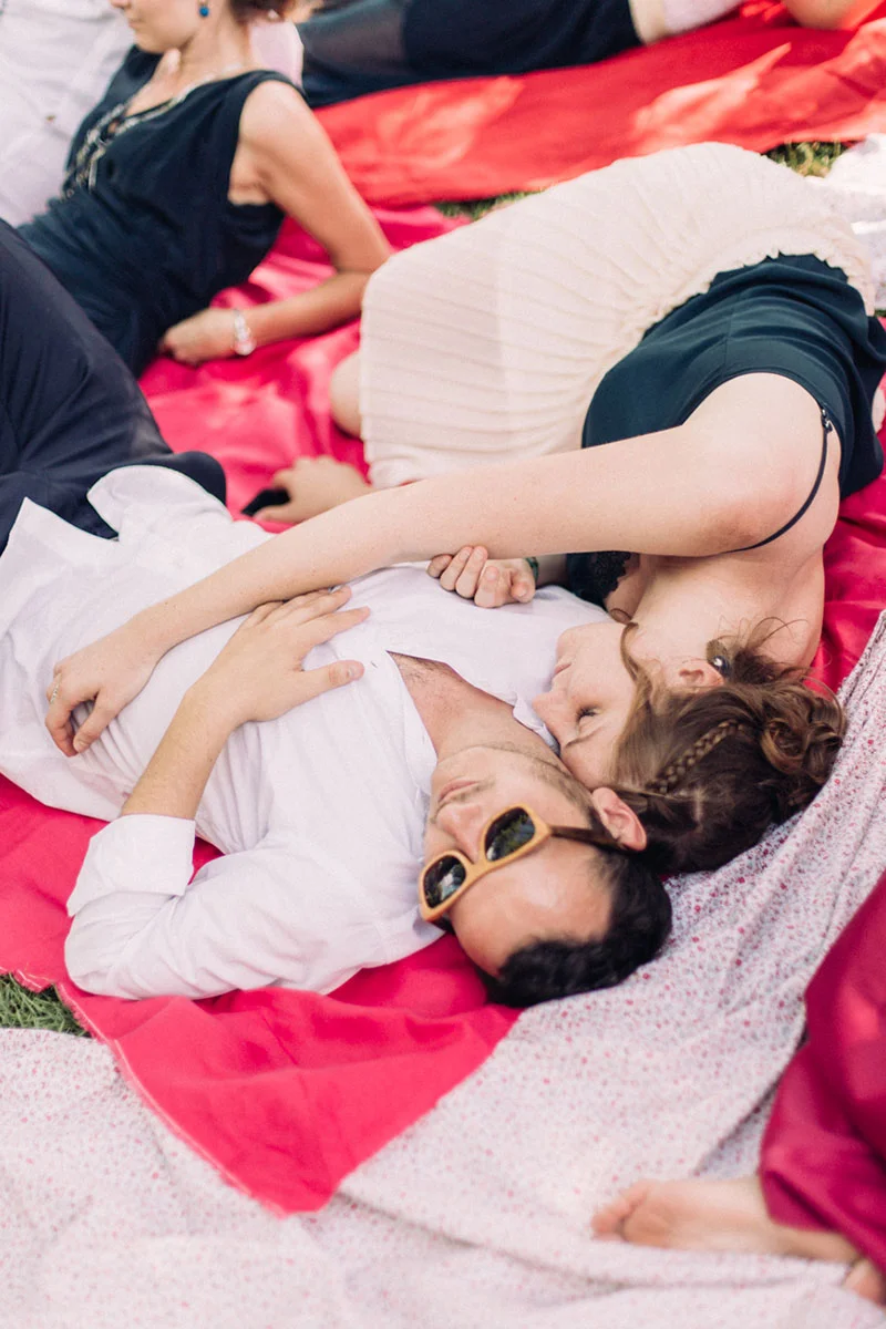 Un couple s'enlace tendrement, allongé sur des couvertures roses lors d'une réception de mariage en plein air.