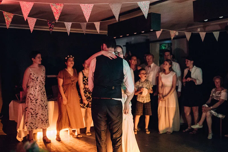 Clara et Julien s'embrassent lors de leur première danse, entourés de leurs invités sous des fanions colorés.