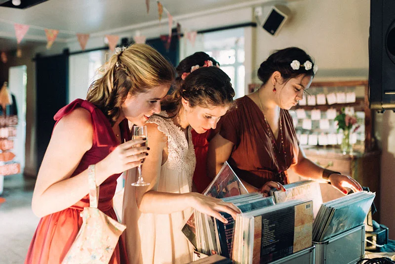 Trois femmes en robes élégantes choisissent des vinyles dans une ambiance festive et chaleureuse.