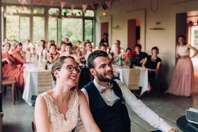 Jeunes mariés souriants entourés de leurs invités lors d'un dîner de mariage convivial et lumineux.