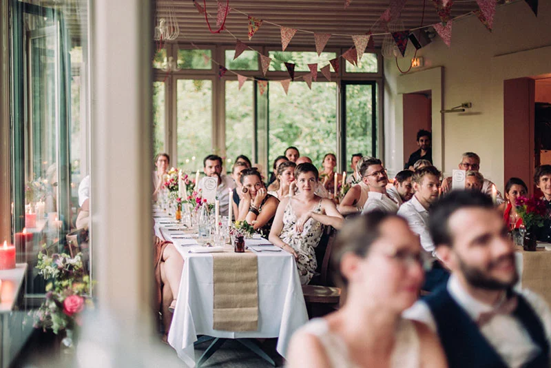 Invités souriants attablés lors d'une réception de mariage conviviale et lumineuse, décorée de fanions colorés.