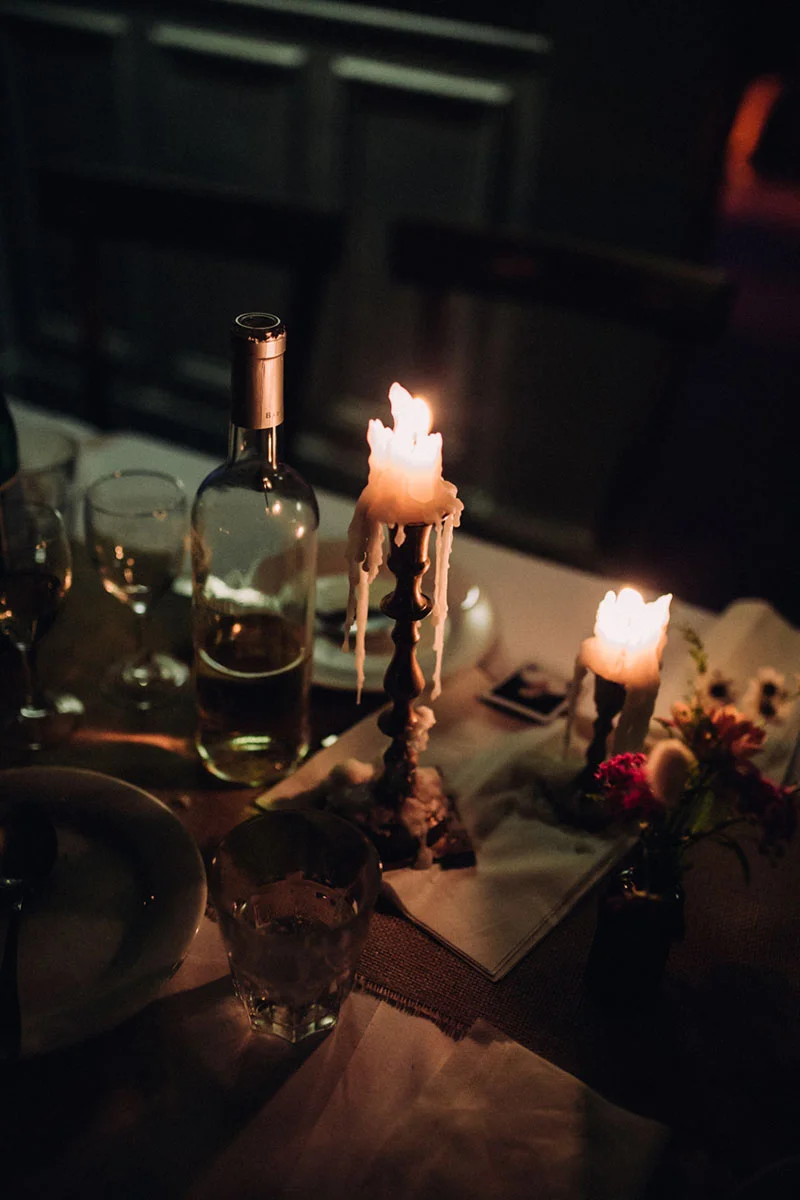 Dîner romantique aux chandelles avec une bouteille de vin et des fleurs, dans une ambiance tamisée et chaleureuse.