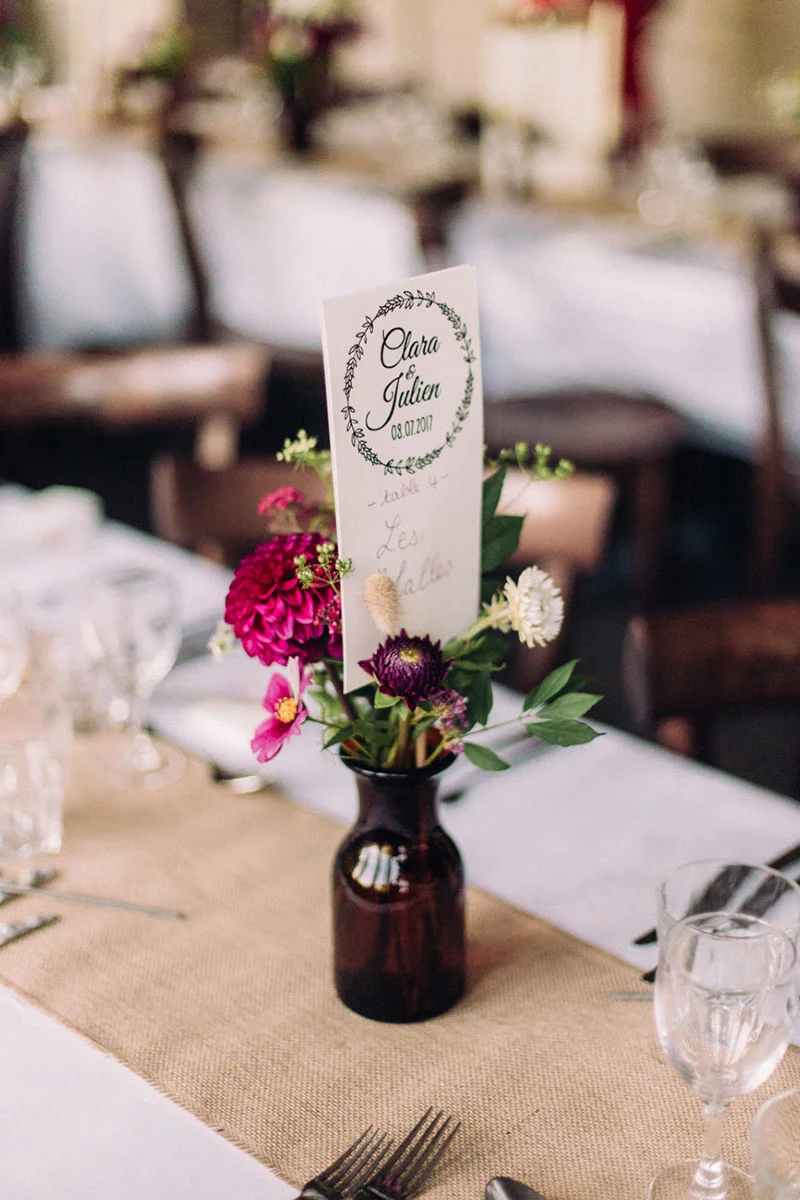 Centre de table champêtre avec fleurs colorées, vase brun et marque-place personnalisé pour Clara et Julien.