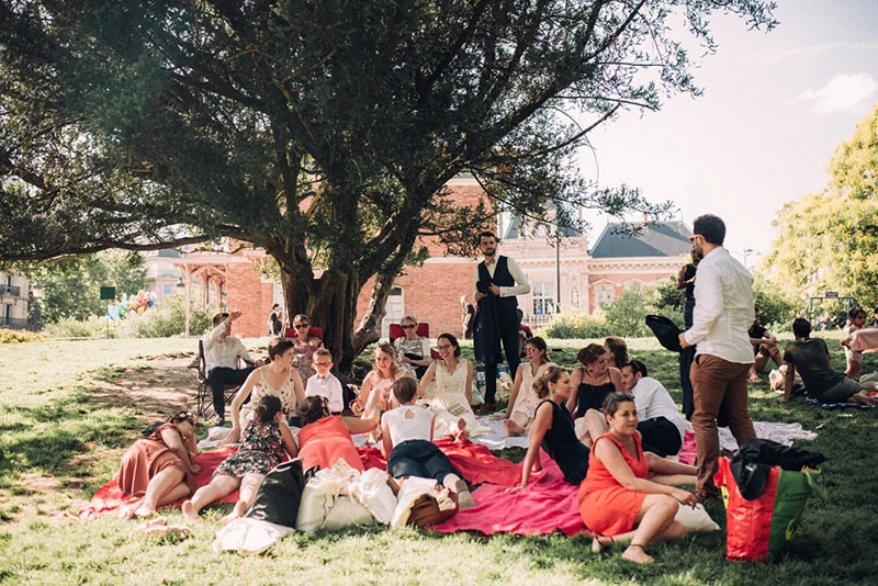 Invités détendus pique-niquant sur des couvertures rouges sous un grand arbre lors du mariage de Clara et Julien.