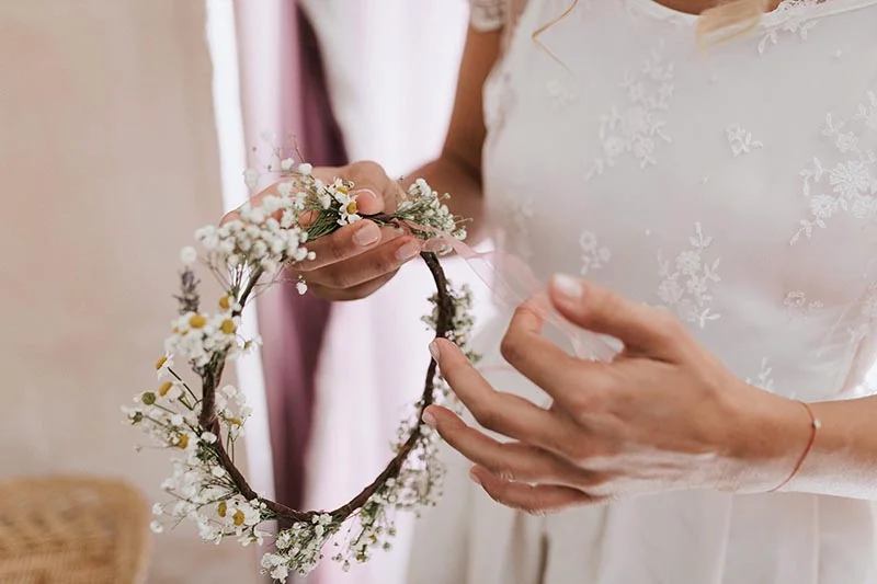 Une mariée en robe blanche tenant une couronne de fleurs blanches et délicates.