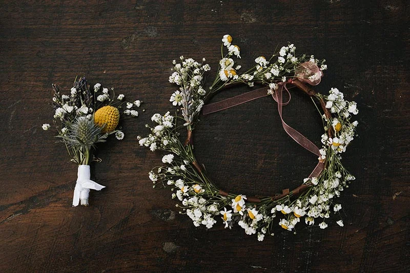 Couronne de fleurs blanches et petit bouquet champêtre posés sur un fond en bois sombre.