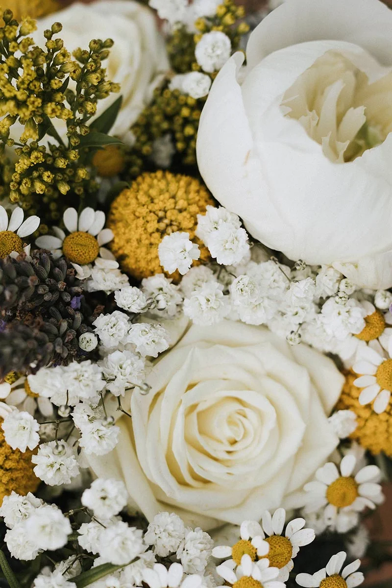 Gros plan d'un bouquet romantique composé de roses blanches, de camomilles et de petites fleurs jaunes et blanches.