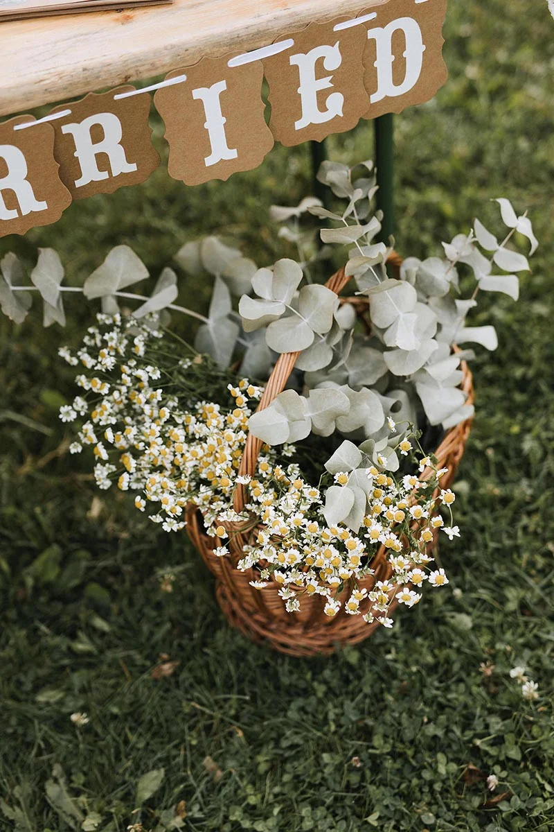 Panier en osier rempli de fleurs blanches et d'eucalyptus posé sur l'herbe sous une bannière Just Married.