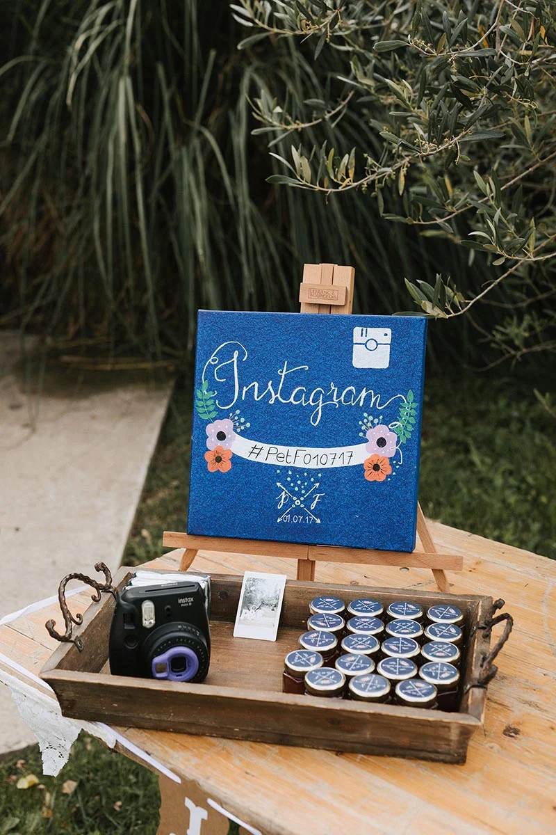 Coin photo de mariage avec un panneau Instagram bleu, un appareil Polaroid et des petits pots de miel sur un plateau.