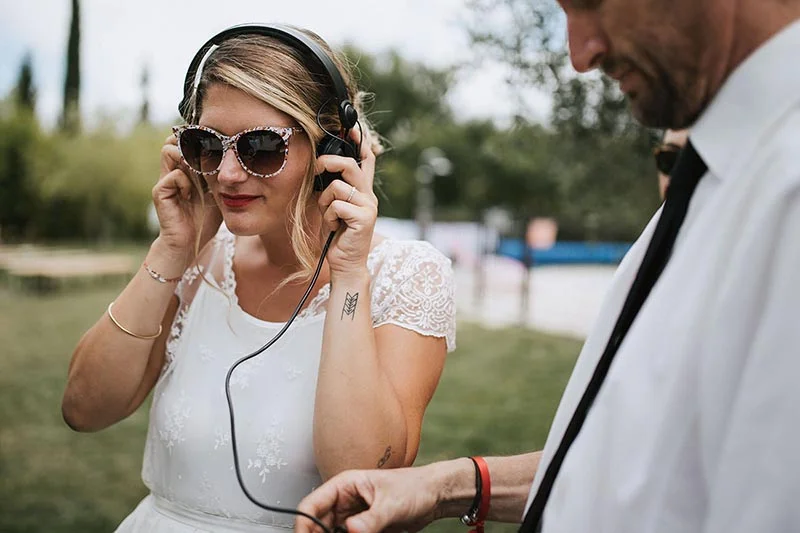 Une mariée en robe blanche et lunettes de soleil portant un casque audio lors de son mariage.