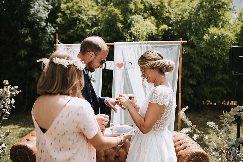 Jeunes mariés s'échangeant les alliances lors d'une cérémonie bohème en extérieur avec un canapé en cuir vintage.