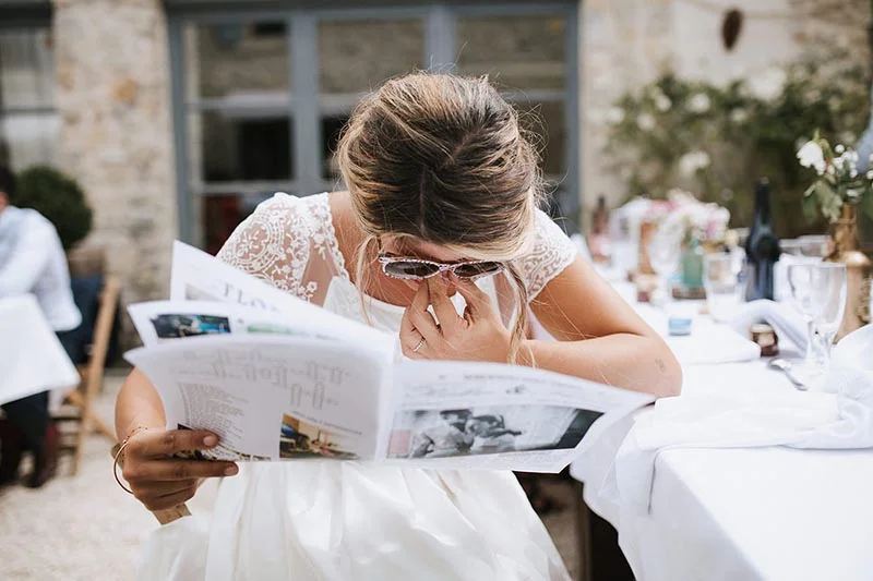 Une mariée en robe blanche, émue, lit un livret de souvenirs lors de son mariage.