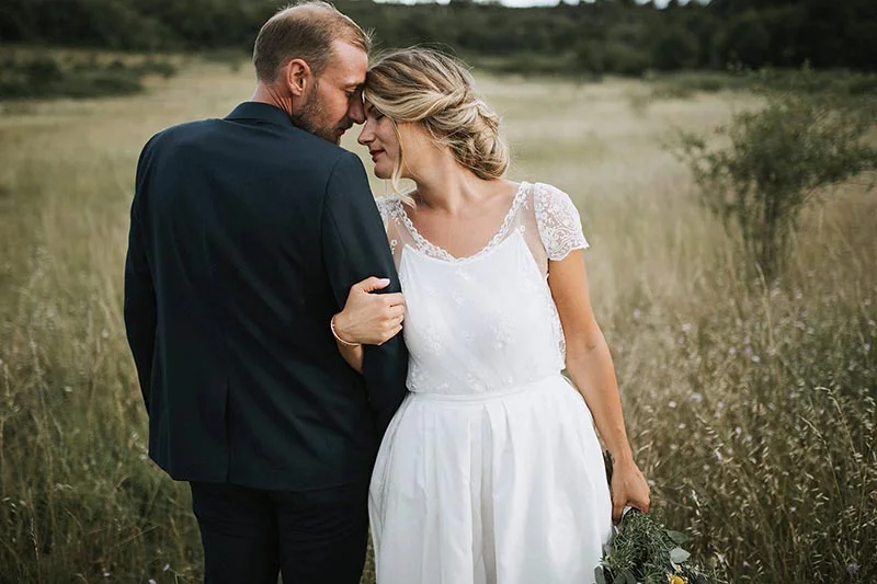 Couple de mariés s'enlaçant tendrement dans un champ sauvage, ambiance romantique et naturelle.