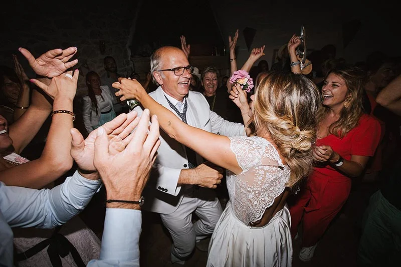 Une mariée en robe blanche danse avec joie entourée d'invités lors d'une soirée festive et animée.