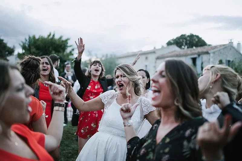 Une mariée et ses invitées chantent et dansent avec enthousiasme lors d'une réception de mariage en extérieur.