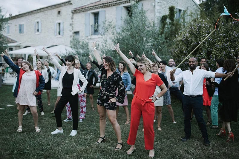 Groupe d'invités joyeux et colorés dansant en plein air devant une bâtisse provençale lors du mariage de Pauline et Florent.