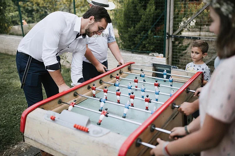Des invités s'amusent autour d'un baby-foot rouge lors du mariage de Pauline et Florent dans un jardin.