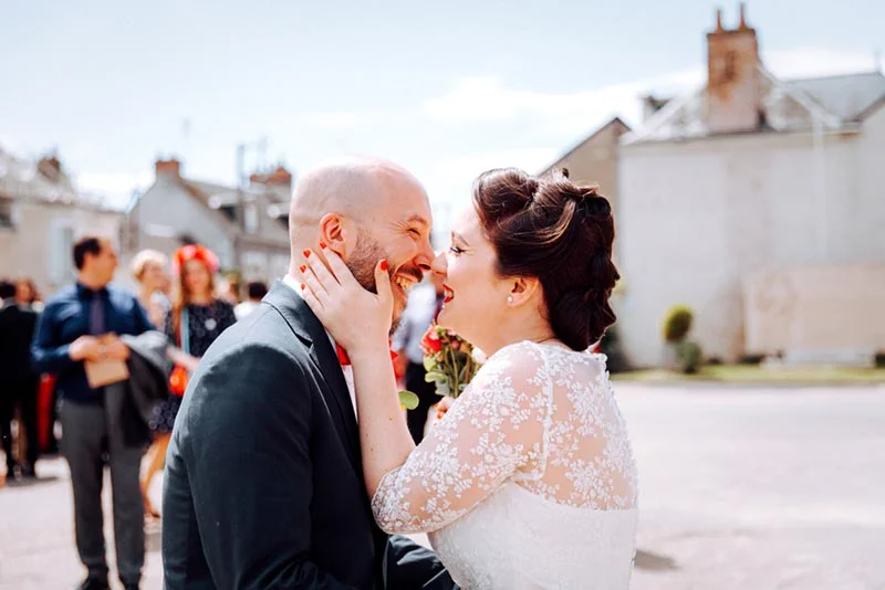 Un couple de mariés s'embrasse tendrement en extérieur, entouré d'invités dans une ambiance lumineuse et joyeuse.