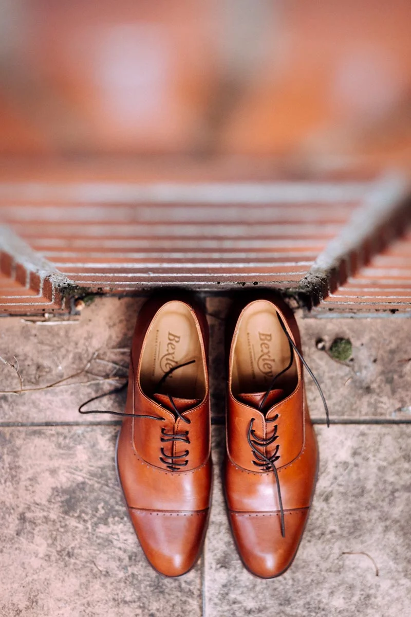 Paire de chaussures richelieu en cuir marron posée sur un sol en pierre devant des marches en briques.