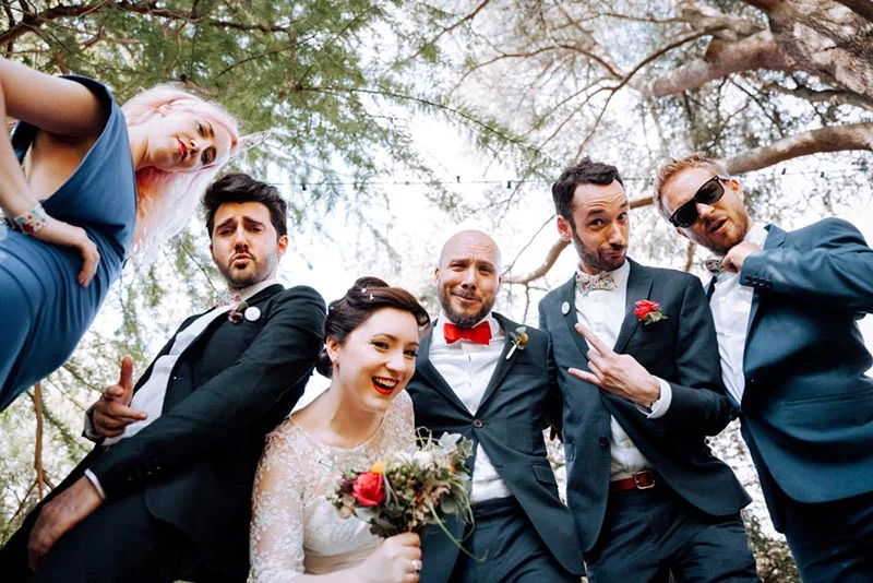 Un groupe d'amis souriants et élégants pose avec complicité en extérieur lors du mariage de Mel et Ben.