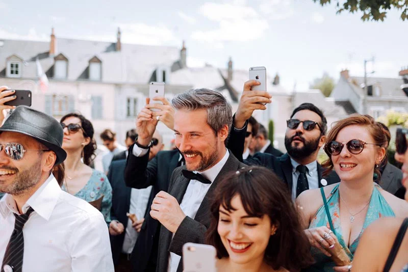 Invités souriants et élégants prenant des photos avec leurs smartphones lors du mariage de Mel et Ben.