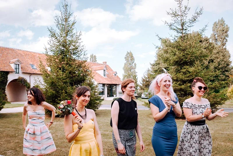 Cinq femmes souriantes en tenues colorées posent dans un jardin devant une maison rustique lors du mariage de Mel & Ben.