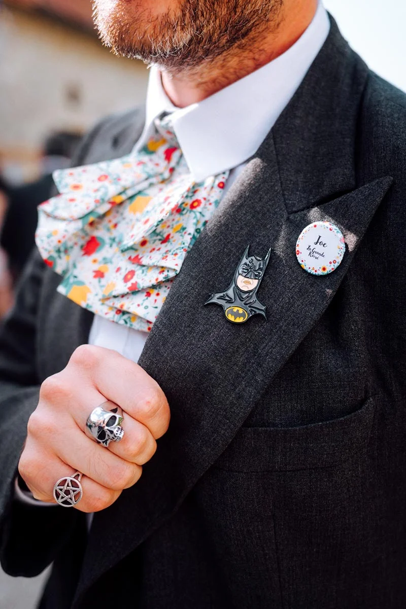 Gros plan d'un marié en costume gris avec un nœud papillon floral coloré et des accessoires originaux.