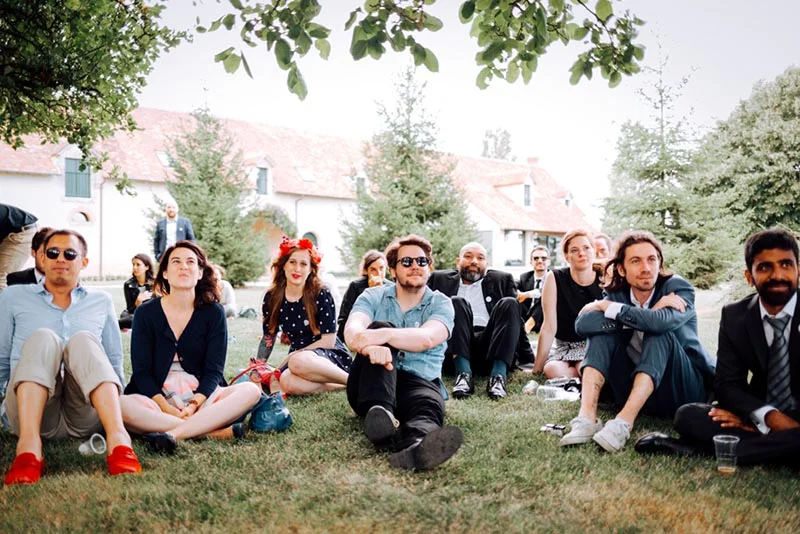 Invités décontractés assis dans l'herbe devant un manoir, lors du mariage de Mel & Ben.