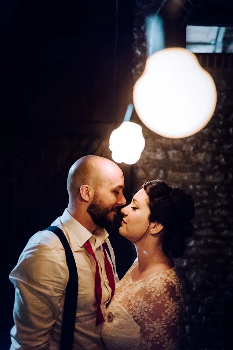Couple de mariés s'embrassant tendrement sous des lumières tamisées dans une ambiance intime et romantique.